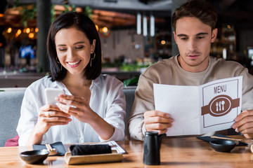 woman smiling while using smartphone near man with menu