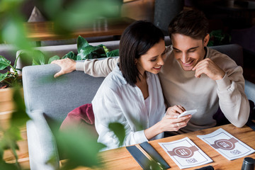 selective focus of happy woman using smartphone near man in sushi bar
