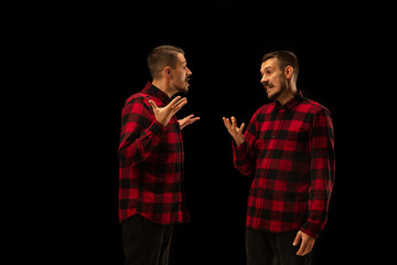 Young handsome man arguing with himself on black studio background. Concept of human emotions,...