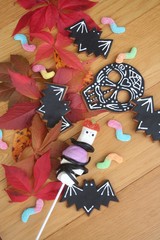Different Halooween sweet food on a wooden table with autumnal leaves. Halloween background with cookies amd candies
