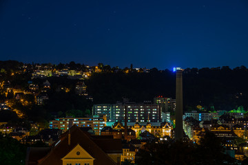 Fototapeta premium Germany, Illuminated houses and roofs aerial view over skyline of stuttgart district heslach by night under starry sky