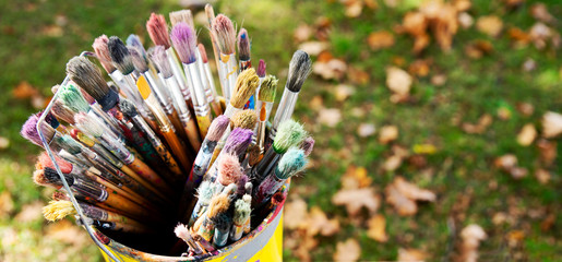 A lot of colorful used brushes in yellow bucket for artistic painting. Equimpent and tool for paint and creative art. Outdoor with brush.