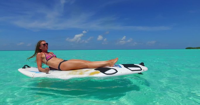 young attractive women relaxing and sunbathing on the paddleboard in aquamarine water of tropical sea with  island in the background. Bikini fashion concept with copy space