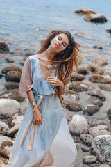 beautiful young fashionable woman in elegant dress posing at the stone beach at sunset