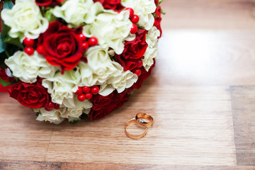 rings and a wedding bouquet of red and white roses on table