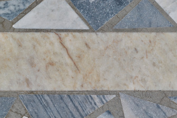 The surface of the floor or wall is made of marble or granite tiles. In the center of the tile rectangular shape. Around the rectangle, the tiles are triangular in shape. The tiles have bands of gray.