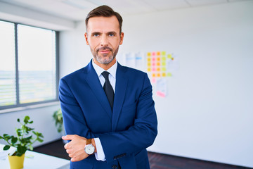 Portrait of handsome businessman standing in office with arms crossed and looking at camera - obrazy, fototapety, plakaty