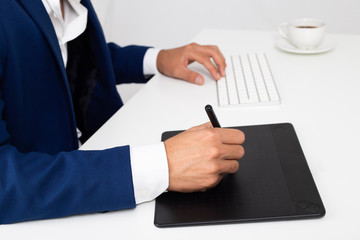 young graphic designer working in his computer in a desktop. He is using a graphic tablet. He is...