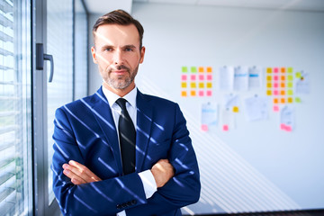 Fototapeta premium Confident businessman standing in office with arms crossed and looking at camera