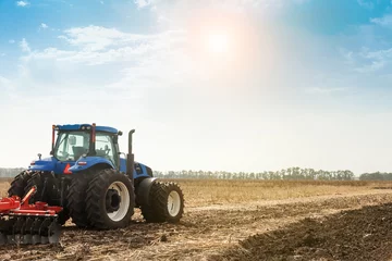 Fotobehang De tractor ploegt het veld, bewerkt de grond voor het zaaien van graan. Het concept van landbouw en landbouwmachines. © murika