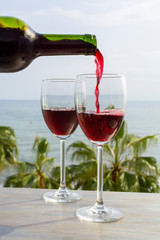 Waiter pouring red wine in glasses in lounge bar with sea view and palm trees