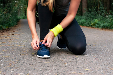 Young tanned blonde girl runner tying shoelaces, getting ready for a run. The concept of a healthy lifestyle, freedom