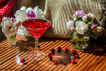 Solemn still life with glass of red drink with autumn berries surrounded by white flowers on a textile background in the diagonal striped shadow of the blinds on a bright sunny day. Greeting card