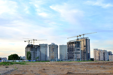 Obraz premium Jib construction tower crane and new residential buildings at a construction site on the sunset and blue sky background - Image