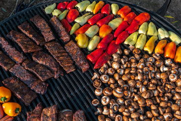 Assorted delicious grilled meat with vegetable on a barbecue with t-bone steak and mushrooms. large rotary grill, field kitchen, food court