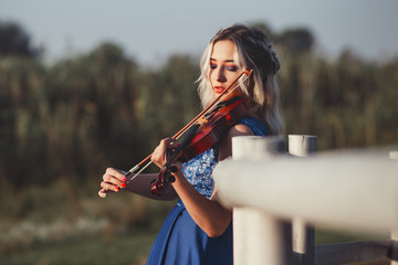 portrait of a beautiful girl in a long dress with a violin near a wooden painted fence, a young woman walks with a musical instrument outdoors © fantom_rd