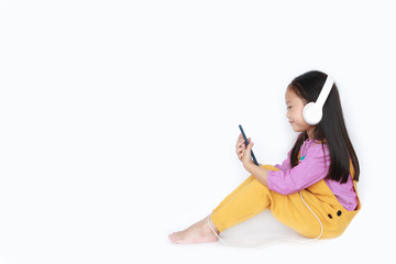 Happy little girl enjoys listening to music with headphones on white background with copy space.