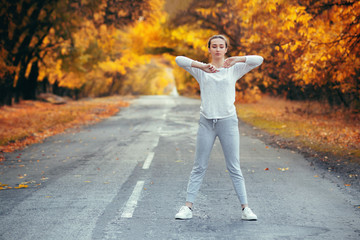 slim young woman in sportswear exercises and warming up on asphalt road, girl engaged in sport outdoors on background of autumn nature, concept health and active lifestyle