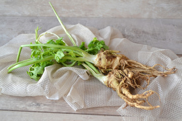 Celery roots with green leaves on a white table with beige napkin