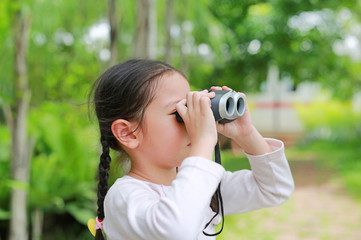 Little child girl in a field looking through binoculars in nature outdoor. Explore and adventure concept.