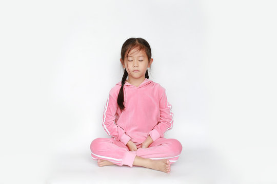 Portrait of beautiful little Asian child girl in pink tracksuit or sport cloth sit in meditation and peace stance over white background. Peaceful concept.