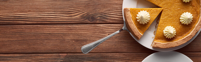 panoramic shot of delicious pumpkin pie with whipped cream on plate with spatula on brown wooden table - obrazy, fototapety, plakaty
