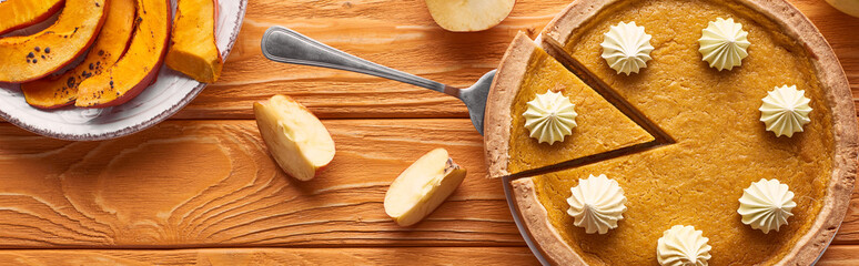 panoramic shot of tasty pumpkin pie with whipped cream near sliced baked pumpkin and cut apple on orange wooden table