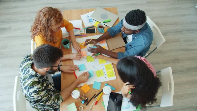 High angle view of young people multi-ethnic group doing collage in office discussing business writing talking sticking paper. Job abd creativity concept.