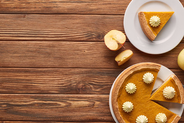 Obraz na płótnie Canvas tasty, cut pumpkin pie with whipped cream near cut apple on brown wooden table