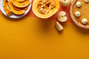 Fototapeta premium delicious pumpkin pie with whipped cream near sliced baked pumpkin, whole and cut apples, and textured napkin on orange surface