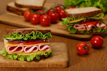 selective focus of fresh sandwich with lettuce, ham, cheese, bacon and tomato on wooden cutting board