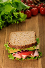 selective focus of fresh sandwich on wooden cutting board near lettuce and cherry tomatoes