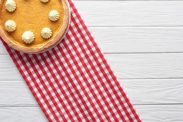 delicious pumpkin pie with whipped cream and checkered napkin on white wooden table