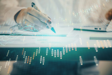 Double exposure of woman's hands making notes with forex graph hologram. Concept technical analysis.