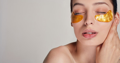 Cosmetic procedures. Facial skin care. Young beautiful girl applying golden collagen patches under...