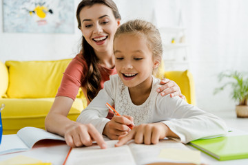  selective focus of happy babysitter and cheerful kid pointing with fingers at book