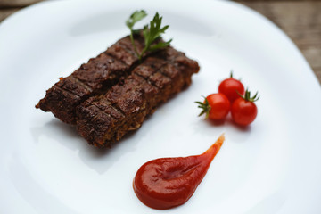 Food in the restaurant. Grilled pork with cherry tomatoes. White plate on a wooden bottom.