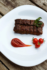 Food in the restaurant. Grilled pork with cherry tomatoes. White plate on a wooden bottom.