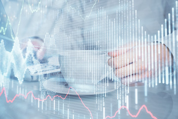 Double exposure of graph with man typing on computer in office on background. Concept of hard work.