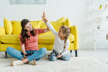 KYIV, UKRAINE - SEPTEMBER 4, 2019: babysitter giving high five to happy kid holding joystick in...