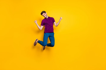 Fototapeta na wymiar Full length body size photo of cheerful positive toothy beaming buy jumping high as rejoicing about having won olympic games wearing blue pants trousers isolated vivid yellow color background