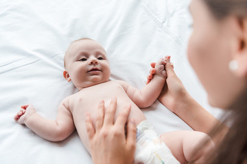 selective focus of caring mother touching cute infant daughter on bed