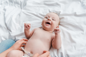 cropped view of mother tickling cheerful baby daughter in diaper