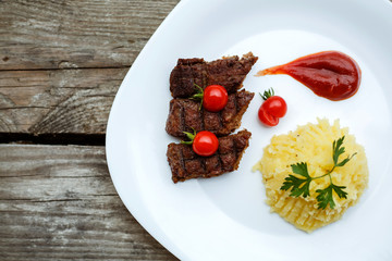 Restaurant food. Pure potatoes combined with grilled pork, decorated with cherry tomatoes. On the wooden floor.