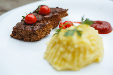 Restaurant food. Pure potatoes combined with grilled pork, decorated with cherry tomatoes. On the wooden floor.