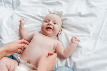 cropped view of mother tickling happy baby daughter in diaper