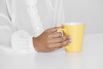 Hand holding yellow cup on a table