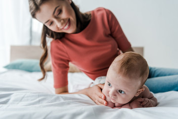 Fototapeta na wymiar selective focus cute infant baby near beautiful mother in bedroom