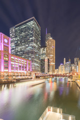 Fototapeta premium Boat tour light trail and Chicago skylines at blue hour with marina cove patio