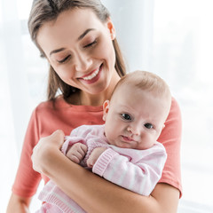 smiling mother holding in arms adorable infant daughter at home